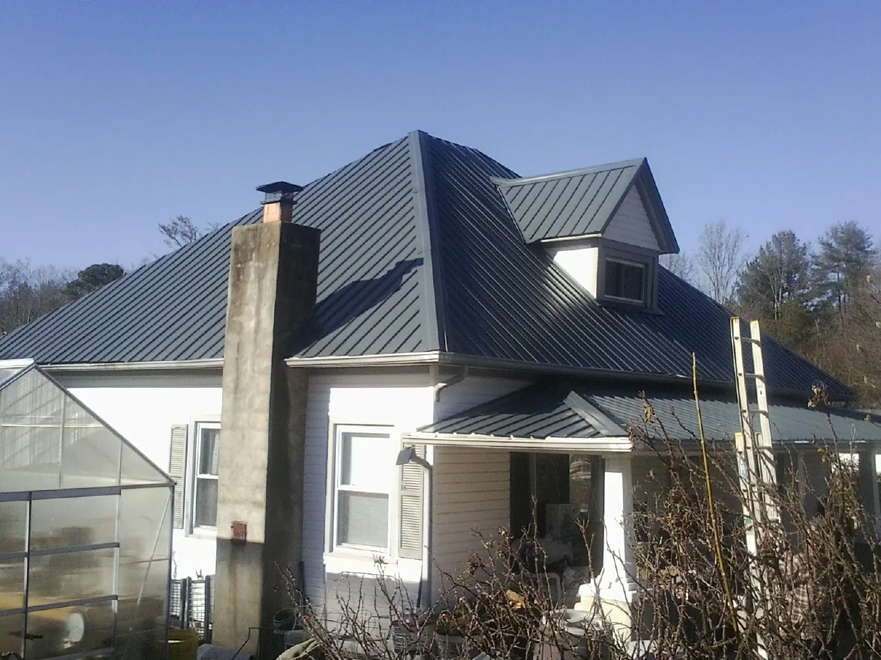 Dark blue standing seam metal roof on a white farmhouse with dormer — Slate & Tile Roof Repair by Roofing Brothers in Laketown
