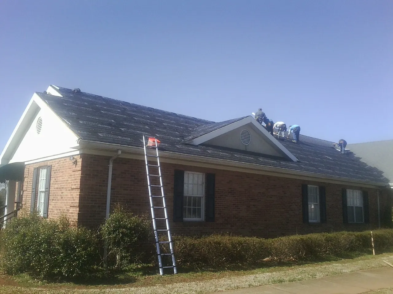 Crew tearing shingles off a brick ranch roof with a ladder set — Emergency Roof Repair work by our crew in Laketown