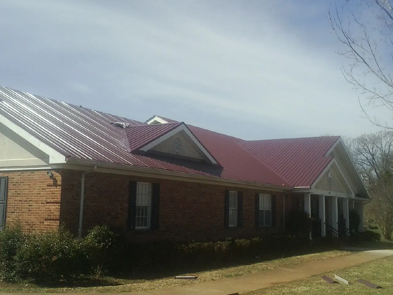 Red metal roof with gabled entries on a long brick building, from a Hail Damage Roof Repair job in Laketown