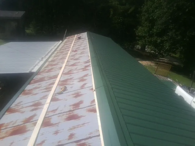 Old rusted panels beside newly installed green metal roofing — Wind Damage Roof Repair by Roofing Brothers in Laketown