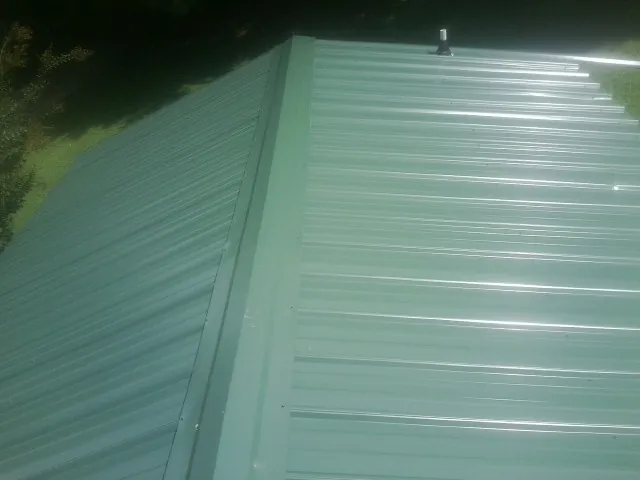 New green metal panels meeting at the ridge of a roof — Flat Roof Repair work by our crew in Laketown