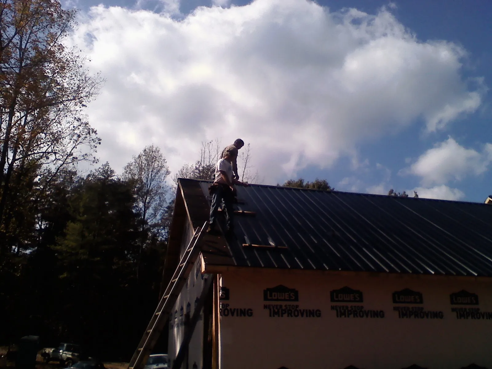 Roofer fastening dark metal panels high against a cloudy sky, from a Roof Inspection job in Laketown