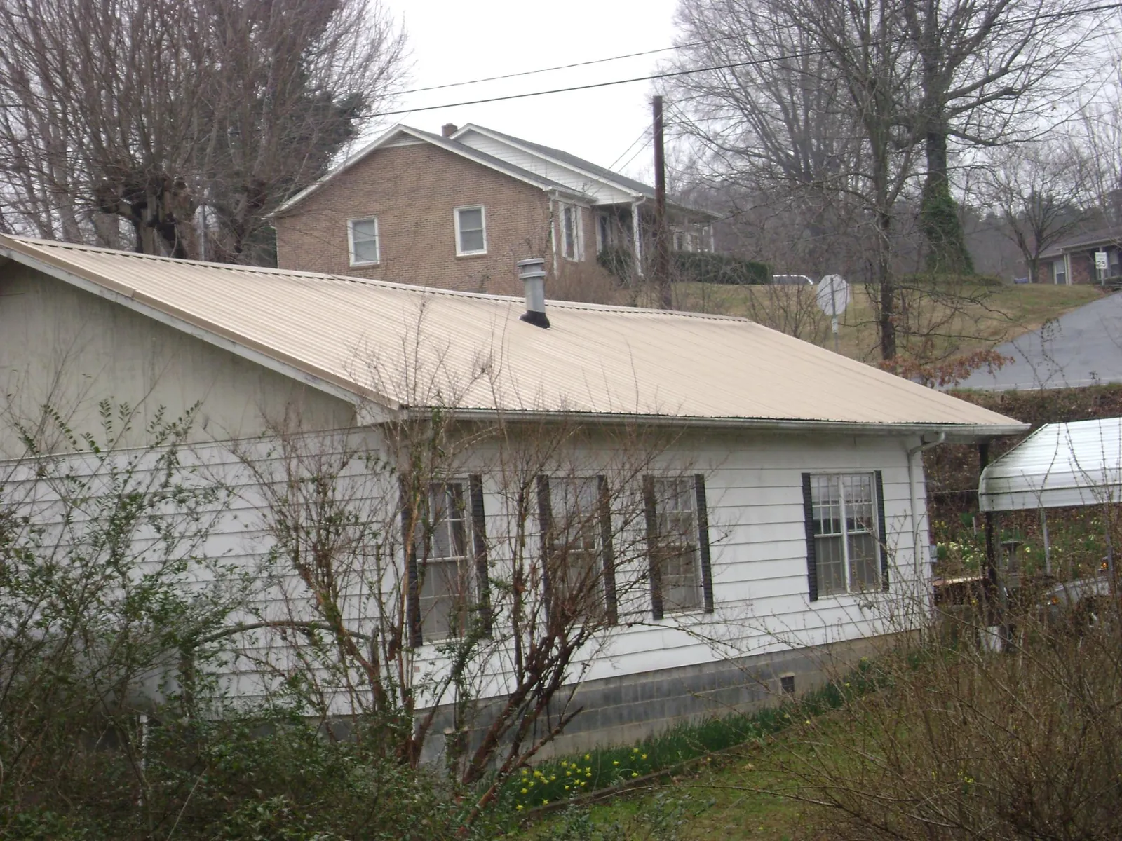 Tan metal roof on a white sided house set into a hillside — Commercial Roofing by Roofing Brothers in Laketown