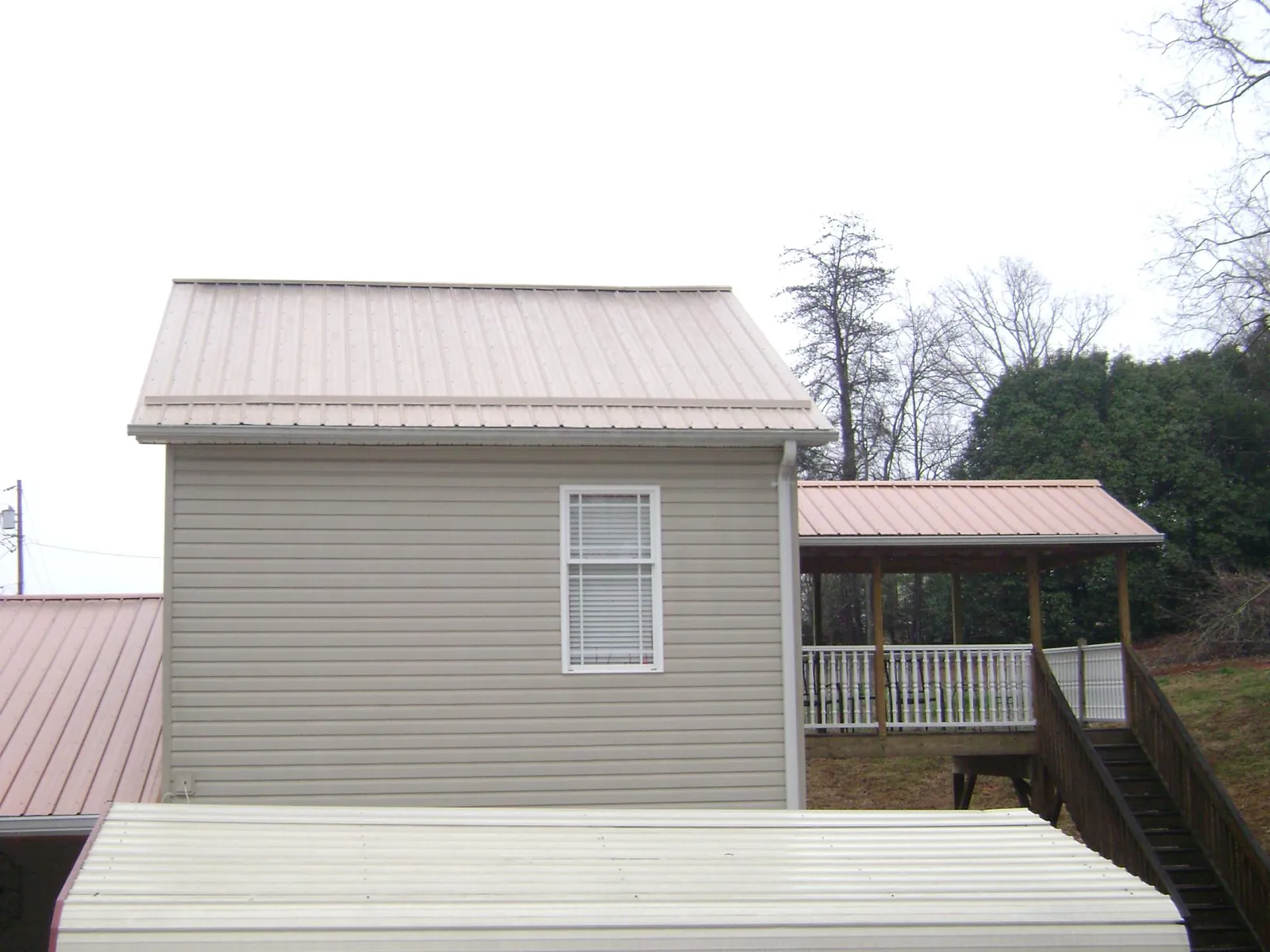 Tan metal roofs on a two story addition and attached porch, from a Roof Replacement job in Laketown